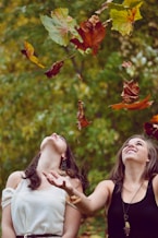 photo of two women throwing leaves during daytime