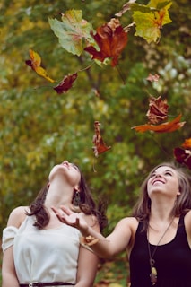photo of two women throwing leaves during daytime