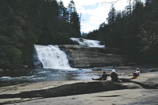 three people sitting on gray surface in front of waterfall in North Carolina United States