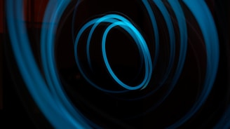 A series of dynamic, swirling blue light trails create circular patterns against a dark background. The light appears to be continuously looping, creating a sense of motion.