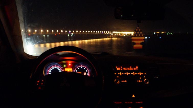 A cozy car interior with a glowing radio display tuned to a lively talk channel, evening city lights visible through the windshield.