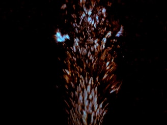 A dark background with a burst of light, possibly representing a cluster of glowing particles or an abstract pattern. The center is illuminated with a mix of bright and dark elements creating a dynamic motion effect.