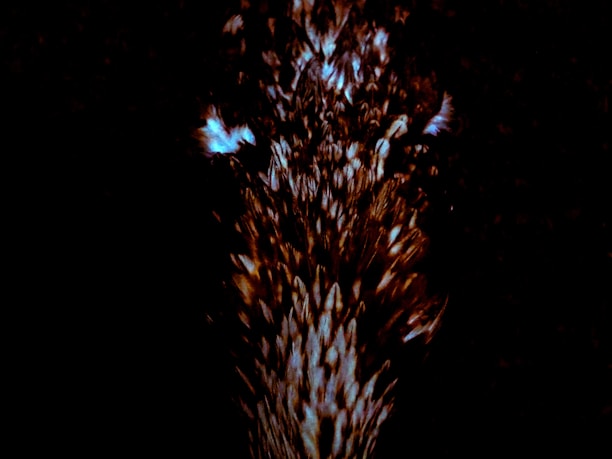 A dark background with a burst of light, possibly representing a cluster of glowing particles or an abstract pattern. The center is illuminated with a mix of bright and dark elements creating a dynamic motion effect.