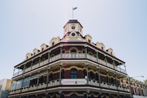 A historic multi-story building with ornate architectural details and a Victorian-style design. The National Hotel features a prominent corner position with wrought-iron balconies, arched windows, and a central tower topped with a flagpole flying a flag.