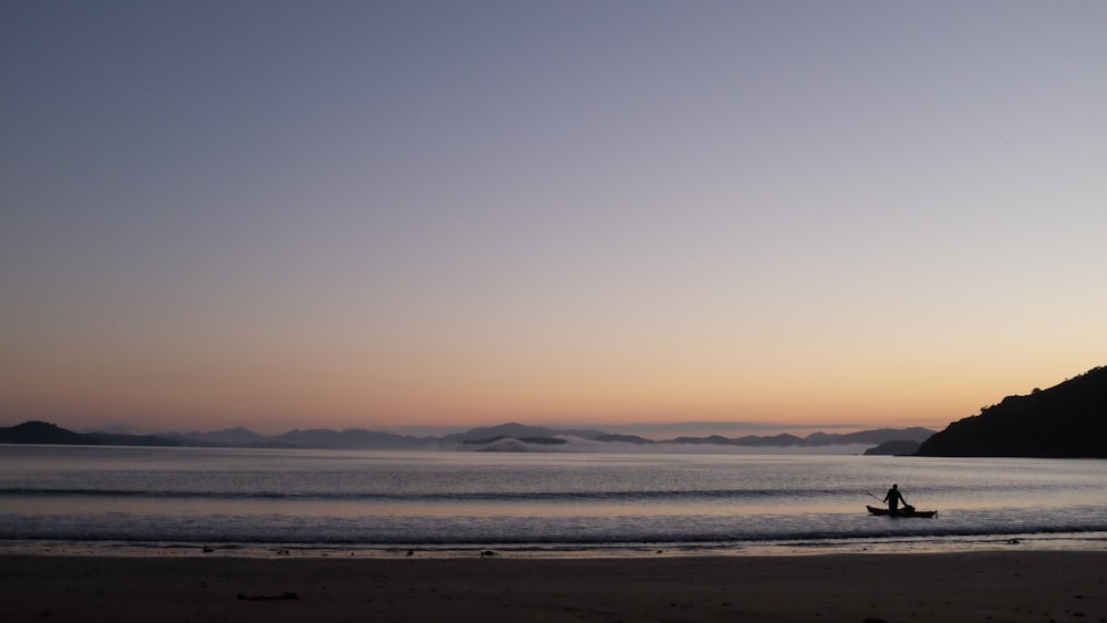 Foto da silhueta da pessoa montada em um menino em mar aberto perto das montanhas durante a hora dourada