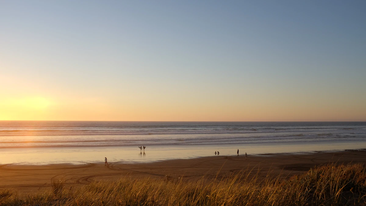 People walking on Ninety Mile Beach at sunset, seen over dune grass