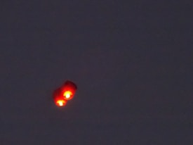 A dark sky with an unidentified flying object emitting a bright red glow with two distinct lights.