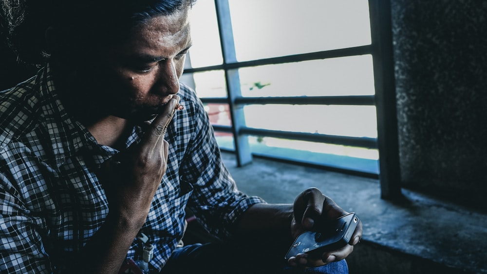 uomo che indossa camicia nera e grigia vicino alla finestra