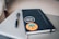 A notebook with a black cover is adorned with two stickers resting on a closed laptop. One sticker reads 'Design makes everything possible' and the other features mountains with the words 'Make stories, leave a trail'. A pen is placed beside the notebook.