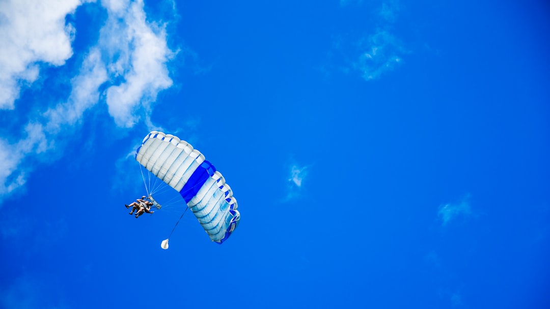 low-angle photography of person riding fan-powered chair with parachute up in sky