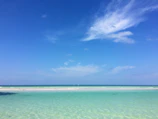 A peaceful beach scene with crystal-clear water and soft white sand under a bright blue sky.