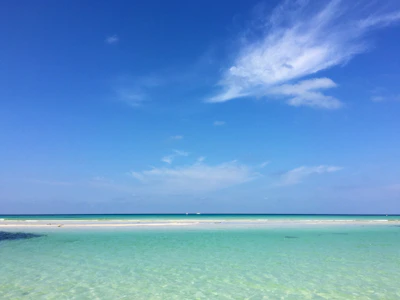 A peaceful beach scene with crystal-clear water and soft white sand under a bright blue sky.