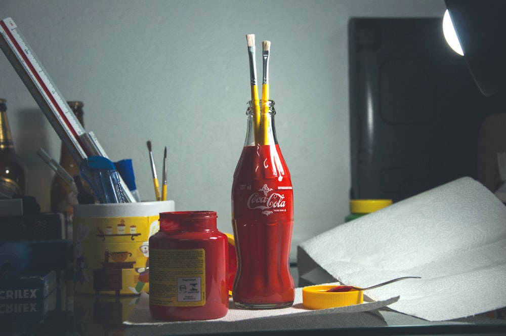 red Coca-Cola glass bottle with paint brushes