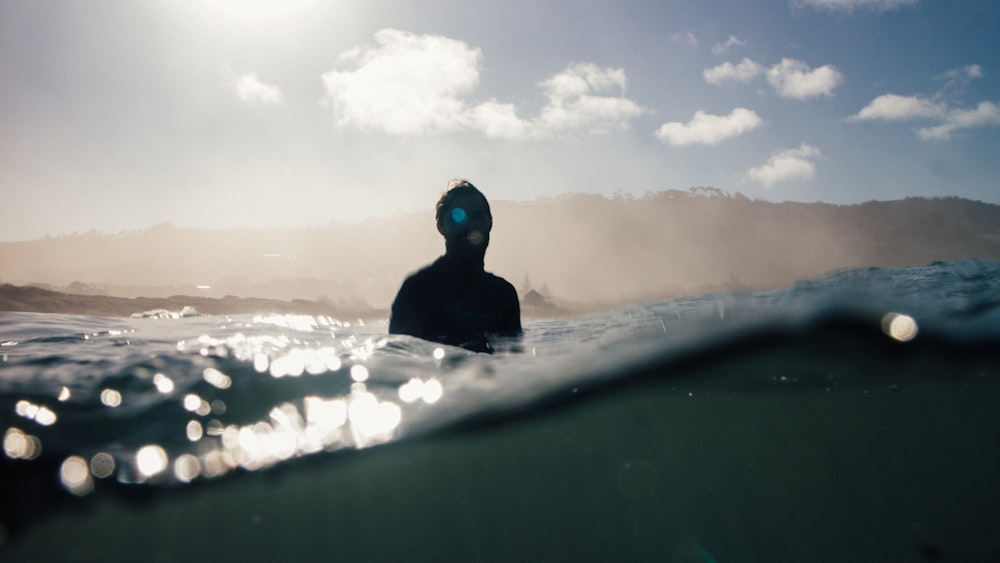 man swimming on body of water near mountain at daytime