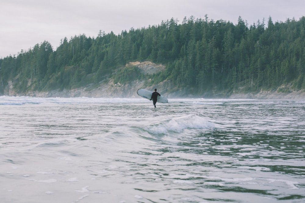 person walking on shore while holding surfboard during daytime