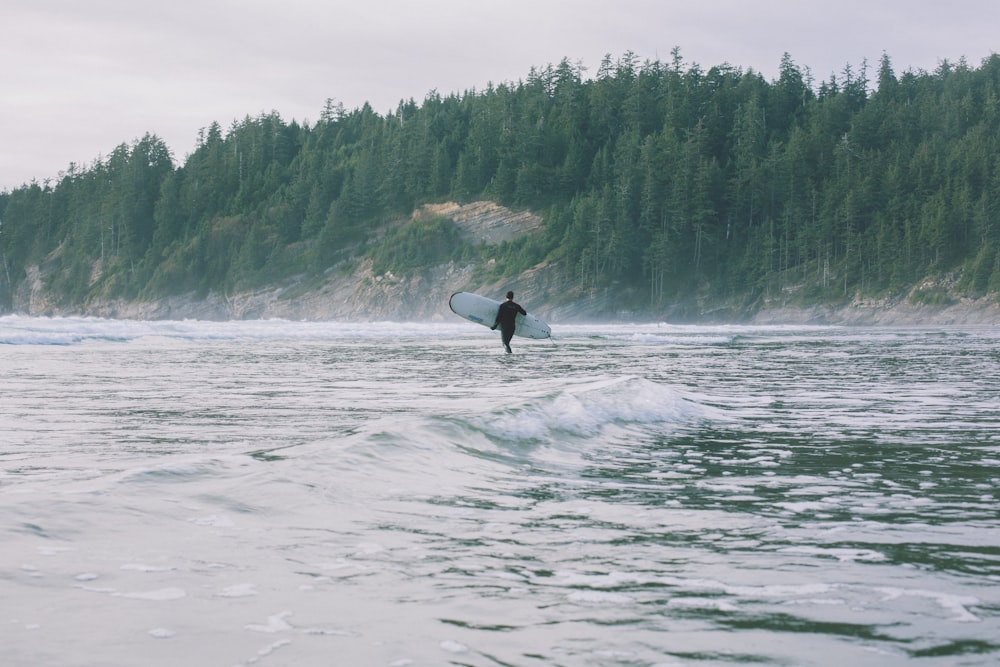 Person, die tagsüber am Ufer spazieren geht, während sie ein Surfbrett hält