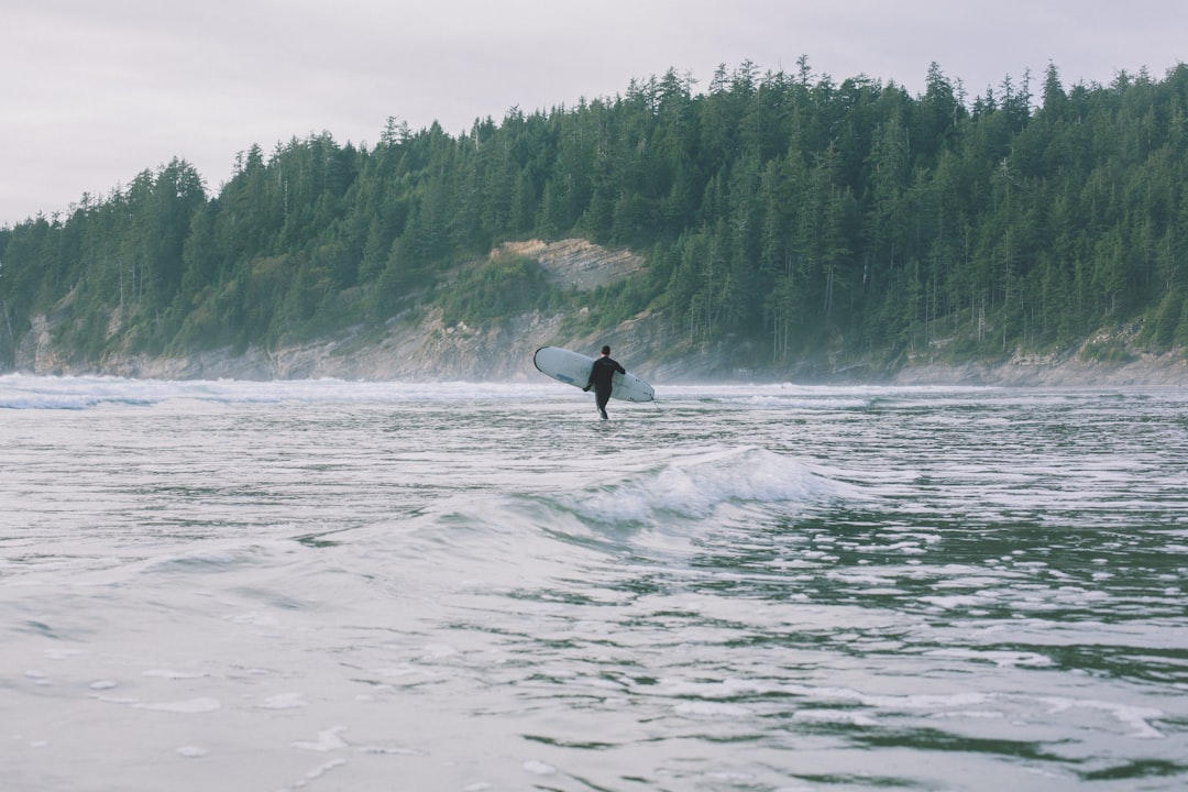 person walking on shore while holding surfboard during daytime