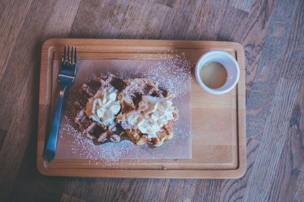 A smiling young woman serving a family a tray of warm waffles topped with whipped cream and berries.