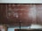 A large, worn out chalkboard filled with complex equations written in white chalk. The equations involve mathematical and physics notations, covering most of the board. The board has a reddish-brown hue with visible wear and scratches.