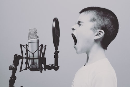 Снимка на момченце пред микрофон, което пее или крещи силно.