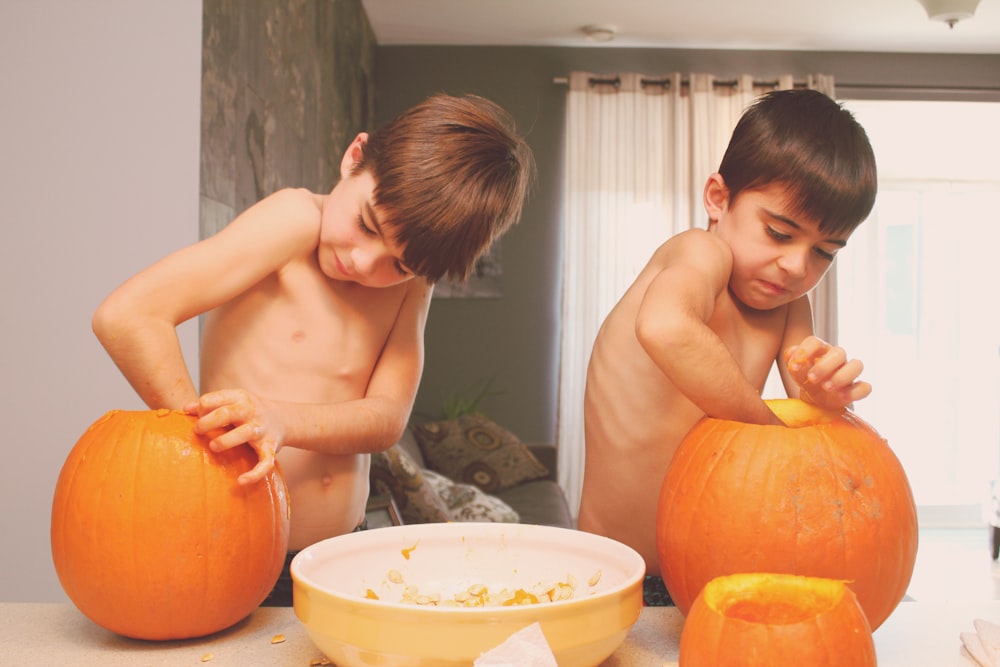 two boys holding pumpkins on table inside house