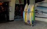 A group of surfers smiling and chatting near a rack of custom surfboards