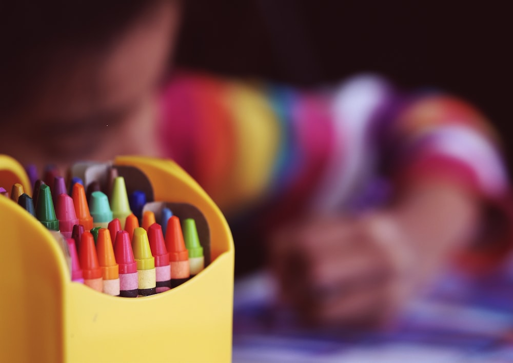 selective focal photo of crayons in yellow box