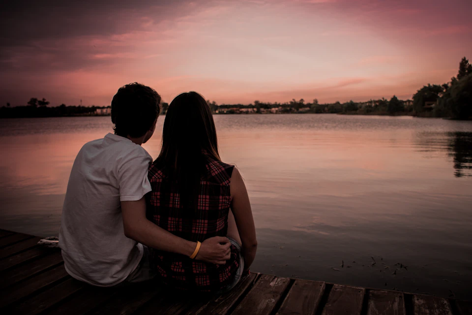 Young couple sits together on wooden dock overlooking serene lake at sunset with golden bracelets