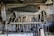 A rustic workshop wall displaying an assortment of vintage woodworking tools. Numerous chisels, saws, and hand drills are organized neatly, with a large hand saw prominently hanging above the rest. A coil of rope is also visible, adding to the aged, well-used feel of the workspace.