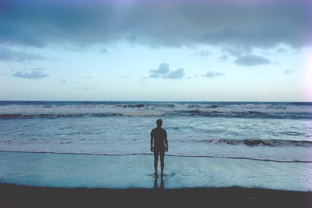 Fotografía de la silueta del hombre de pie en la orilla del mar