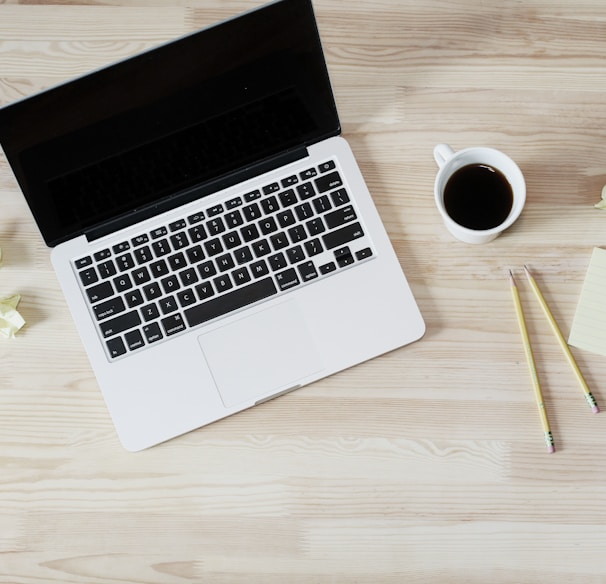 turned off MacBook Pro beside white ceramic mug filled with coffee