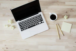 A desk with printed worksheets, a pen, and a coffee cup beside a laptop.