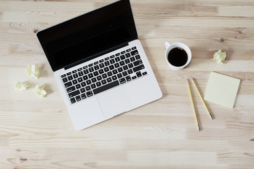 A close-up of a writer's desk with a laptop, notes, and a cup of coffee.