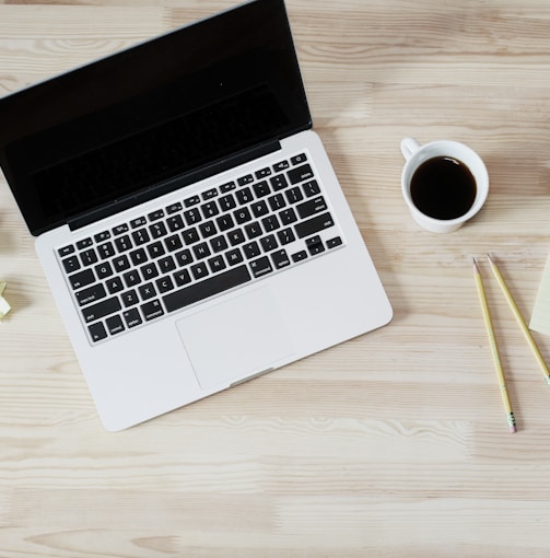 turned off MacBook Pro beside white ceramic mug filled with coffee