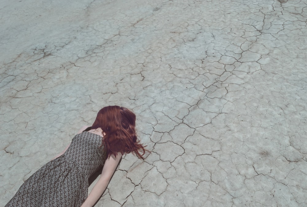 Woman with hair over face lying down on cracked desert floor