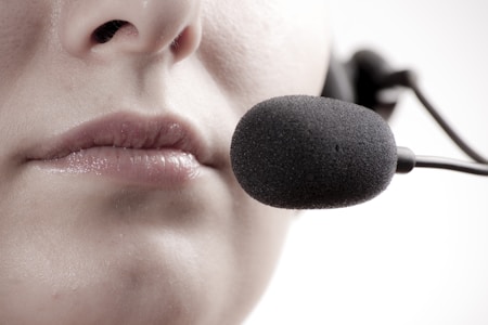 A close-up of a person's lips speaking into a black microphone headset, suggesting communication or recording.