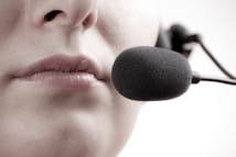 A close-up of a person's lips speaking into a black microphone headset, suggesting communication or recording.