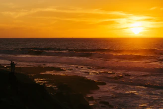 A vibrant photo of a traveler standing on a cliff overlooking a colorful sunset over the ocean, capturing the spirit of adventure.
