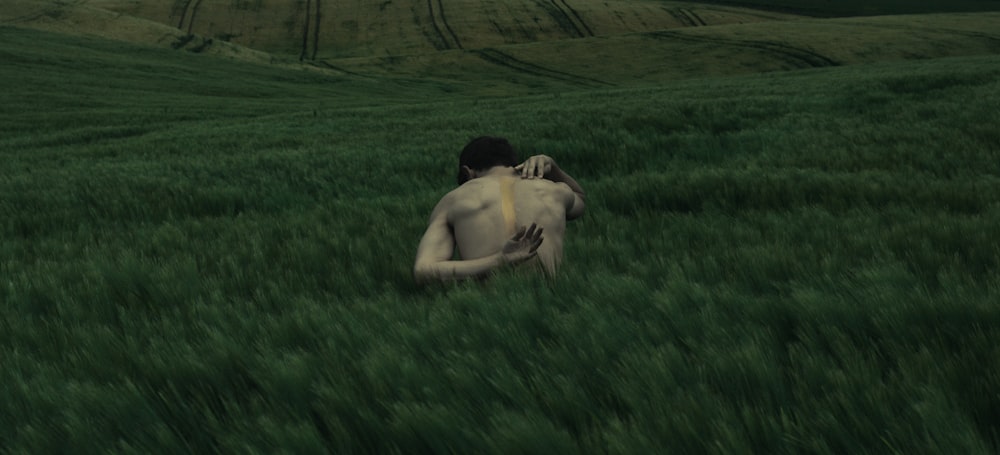 Una persona a torso nudo che si gratta la schiena in un campo di erba alta.