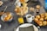 A table is set with an array of breakfast items, including croissants in a metal bowl, sliced baguette in a basket, glasses of orange juice, and a cup of coffee. Three lit candles add warmth to the setting. There are also cheese-topped savory pastries on a black plate.