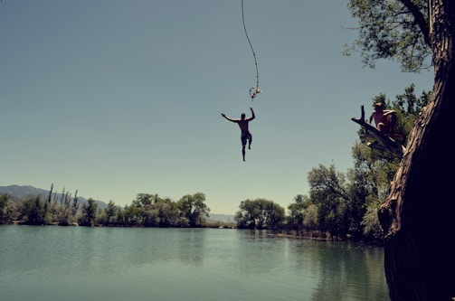 man jumping on body of water with rope