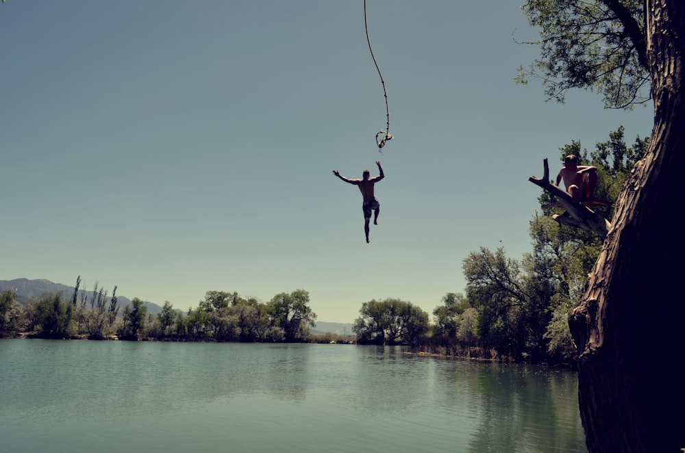 homem pulando no corpo de água com corda