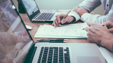 person holding pencil near laptop computer