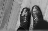 Close-up of handcrafted black boots resting on a vintage wooden floor with soft natural light.