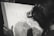 A person is engaged in a detailed drawing, focusing intently on the artwork. The drawing features intricate designs of flora and fauna, suggesting a theme of nature. The image is in black and white, enhancing the focus on the pencil work and the concentration of the artist.