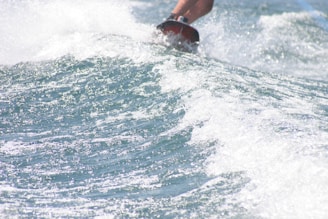 Close-up of a surfboard slicing through crystal-clear ocean waves under a bright blue sky.