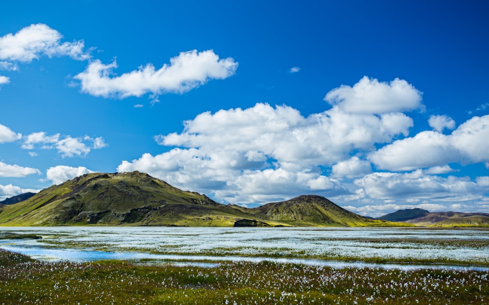 brown mountain near body of water under clear blue and white sky