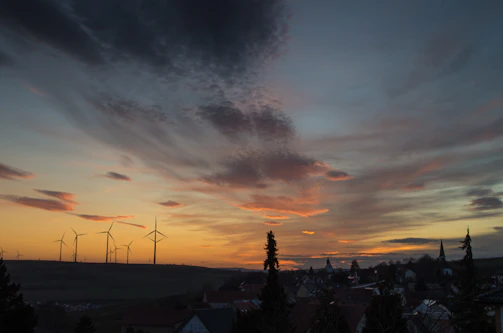A panoramic view of a wind farm at sunset with turbines turning gently against a colorful sky