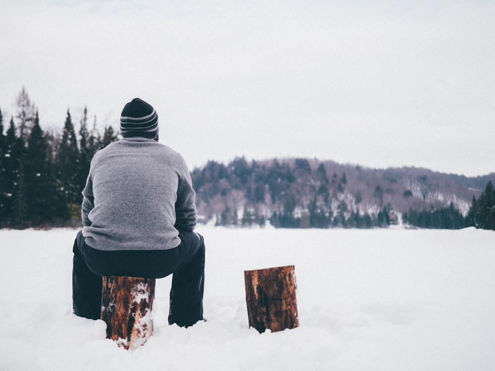 겨울에 통나무에 앉아있는 회색 스웨터를 입은 남자