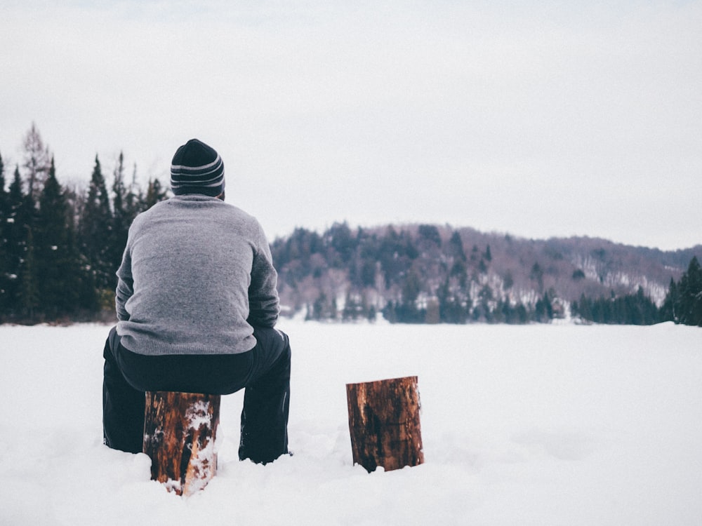 Mann mit grauem Pullover sitzt im Winter auf Baumstamm